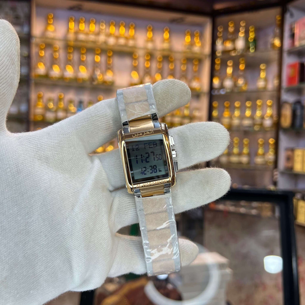 Gold and silver digital watch held by a gloved hand with a jewelry store background.