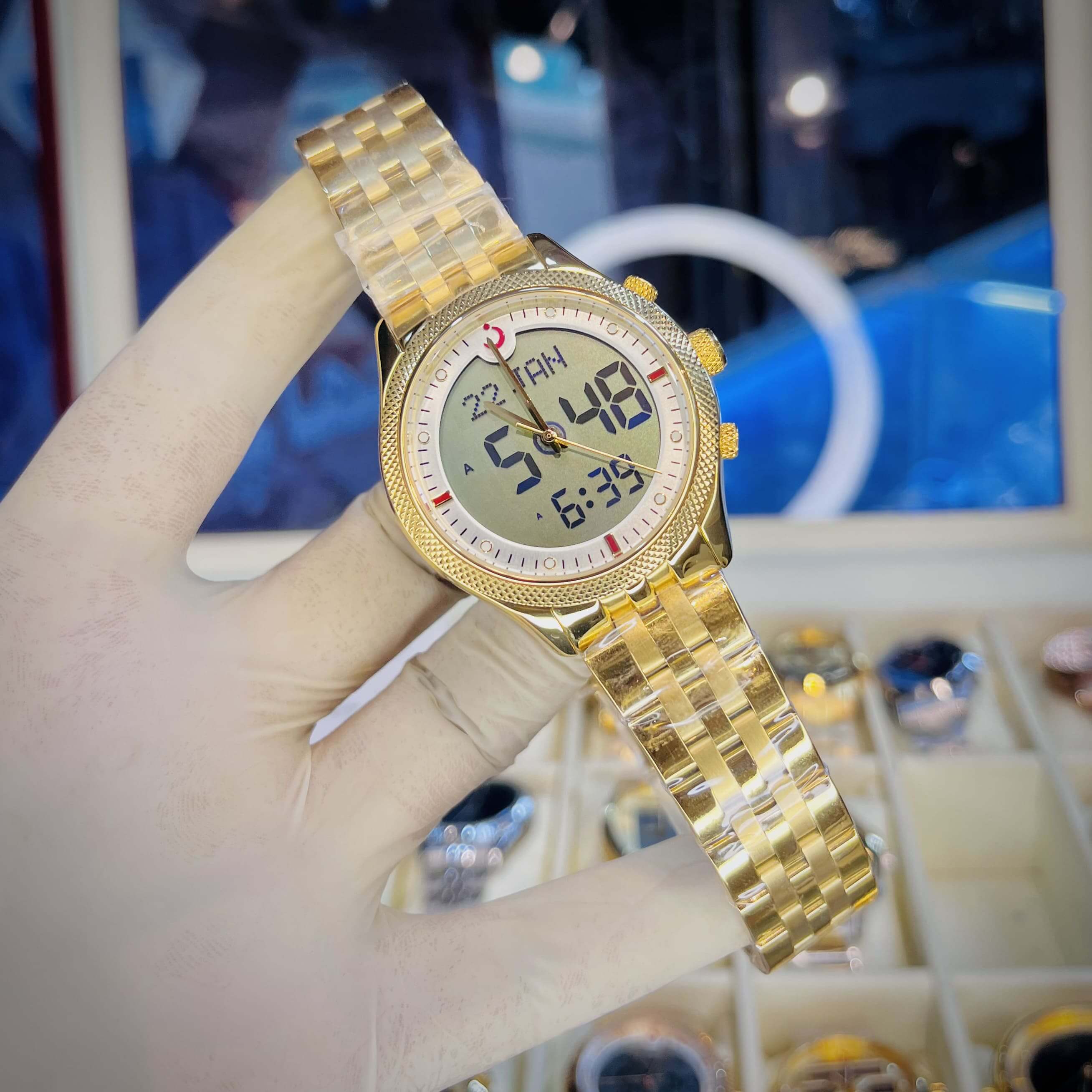 Gold wristwatch with digital display held by a gloved hand against a blurred background