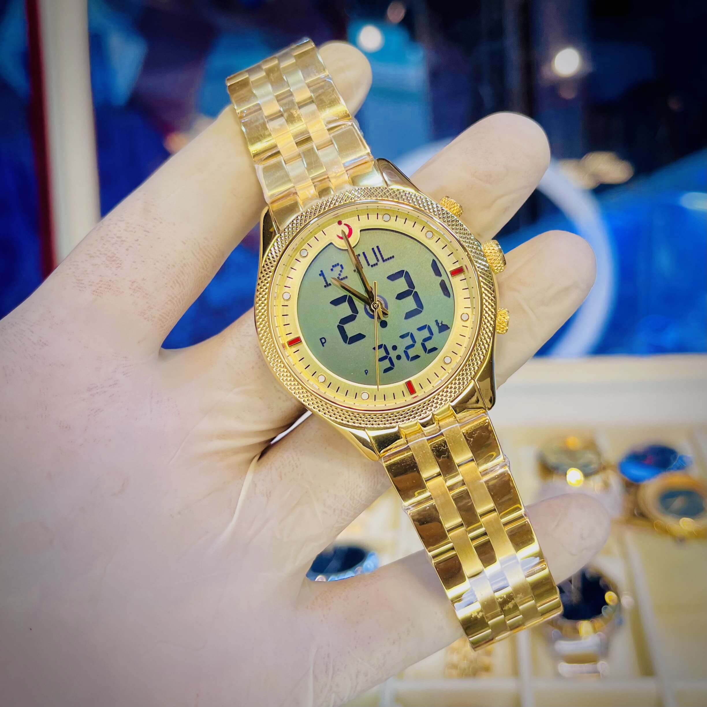 Gold wristwatch with digital display held in a hand against a blurred background