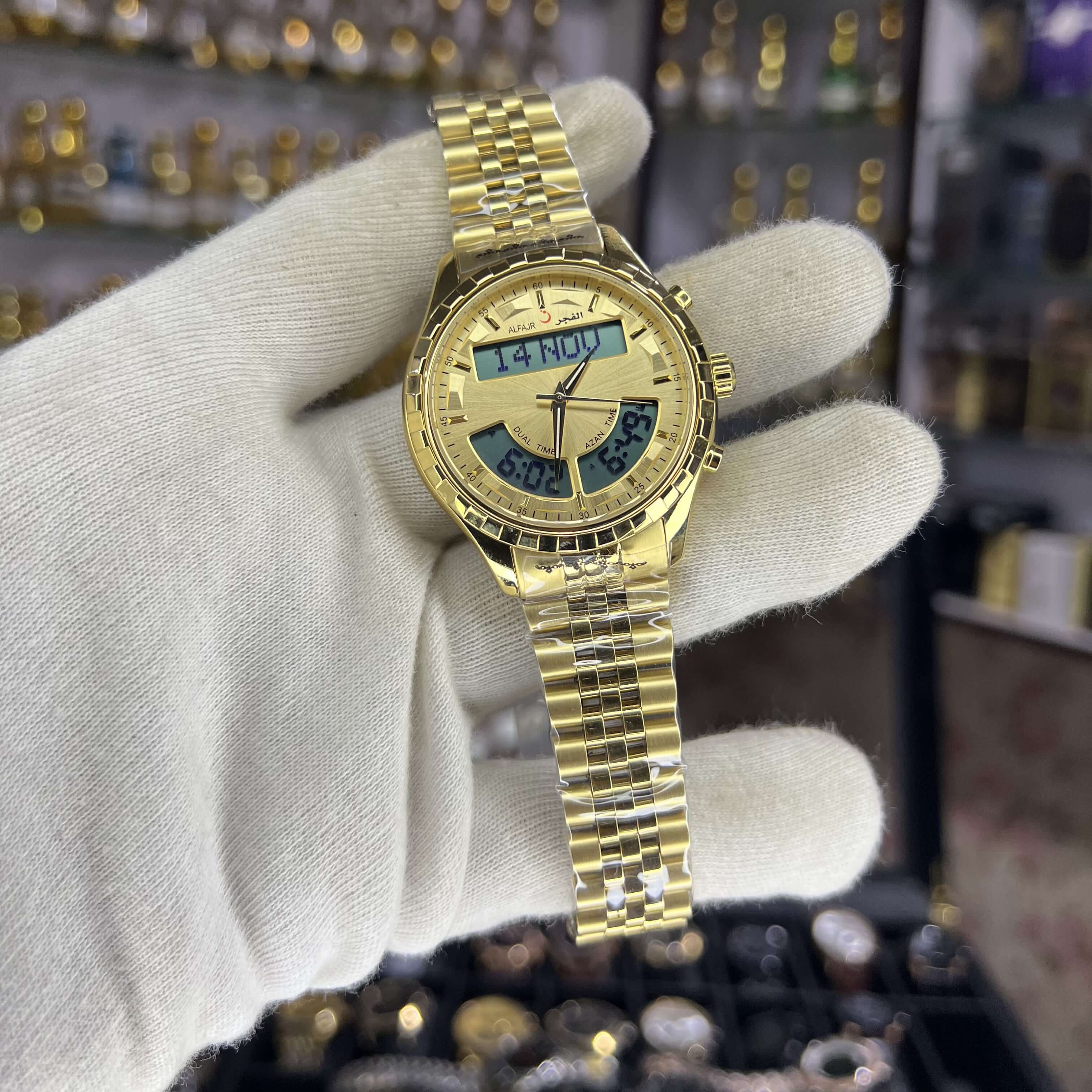 Gold wristwatch held by a gloved hand with a blurred background of jewelry display.