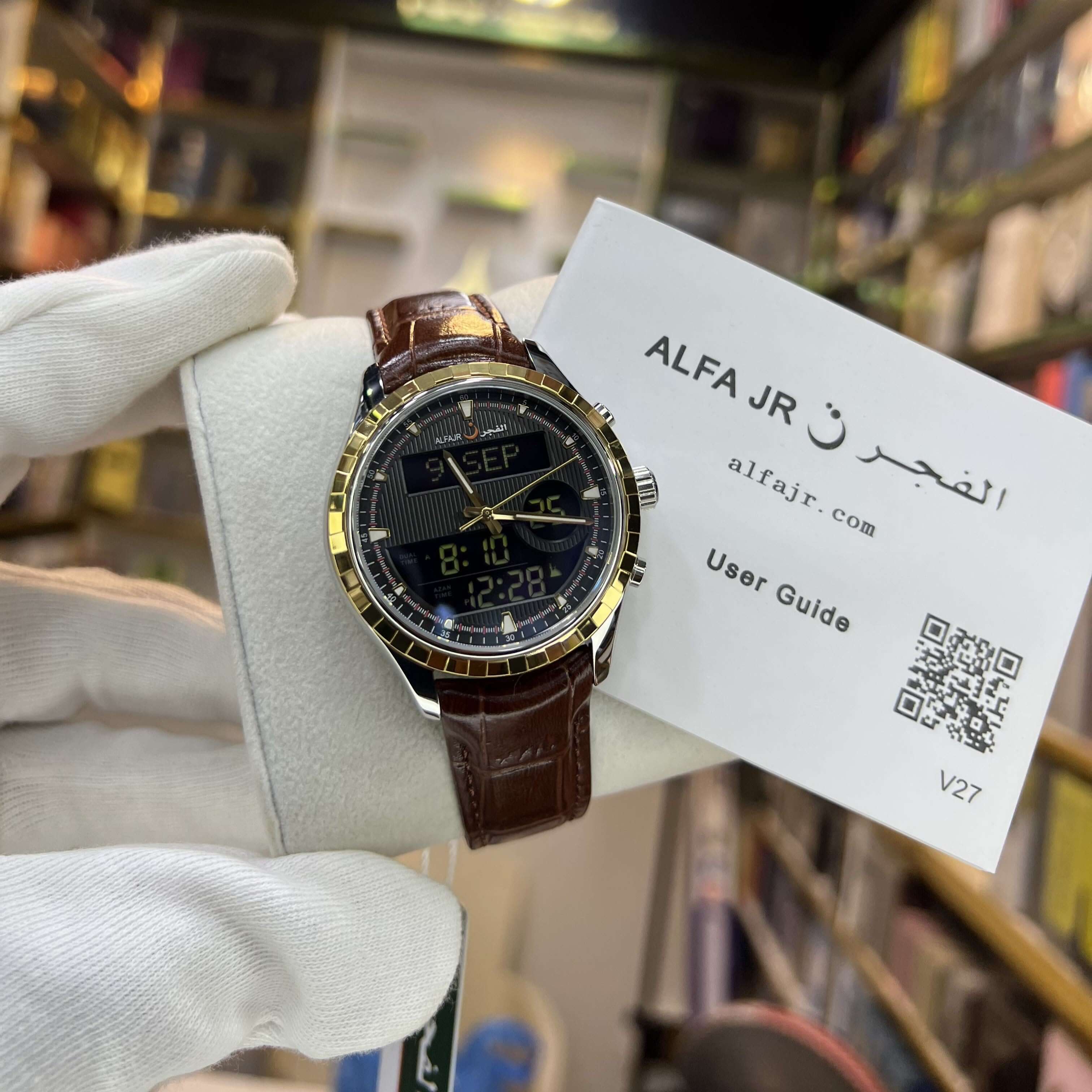 Watch with brown leather strap held by a gloved hand, accompanied by an 'ALFA JR' user guide.