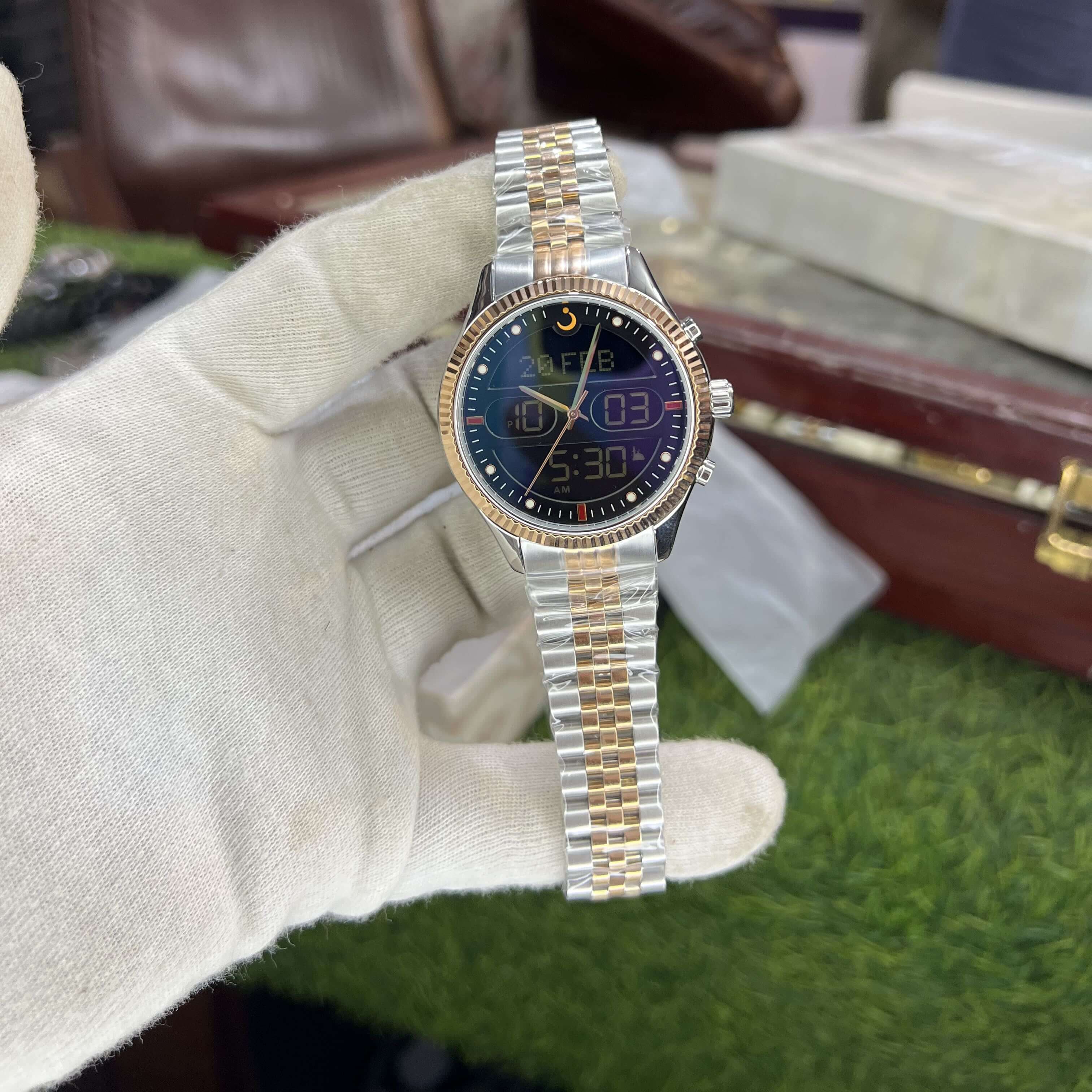 Two-tone watch held by a gloved hand with a blurred background