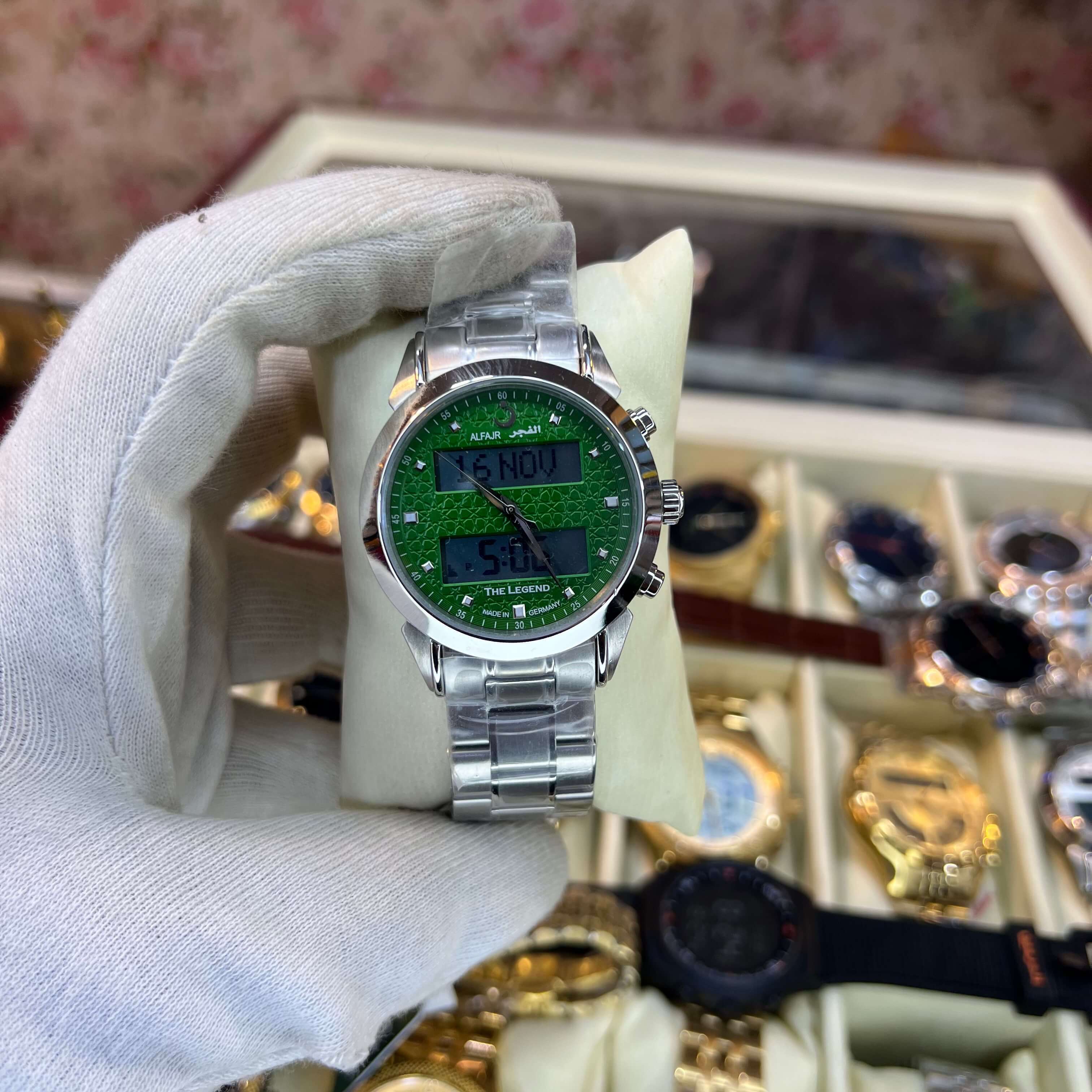 Watch with green face and silver case held by a gloved hand, 
