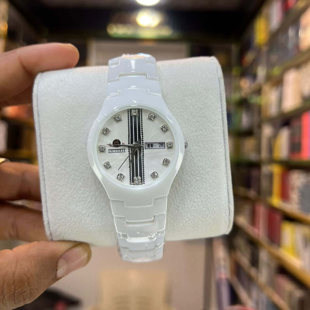 White watch with diamond-like stones on a white cushion, held in front of a bookshelf.