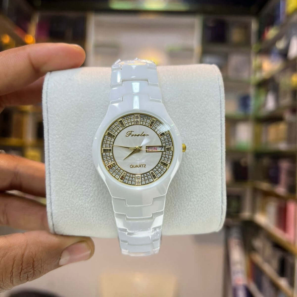 White watch with decorative face held in a hand against a blurred background